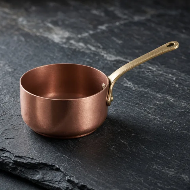 Unbranded copper saucepan with a brass handle on slate
